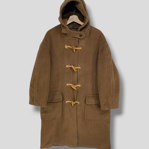 Può includere: Un montgomery marrone con cappuccio e chiusure a toggle in legno. Il cappotto ha due tasche anteriori e una chiusura con bottone sul colletto. Il cappotto è realizzato in un tessuto spesso e strutturato.