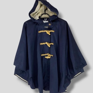 May include: A navy blue hooded poncho with wooden toggle closures. The poncho has a cream-colored lining in the hood and is hanging on a black hanger. The poncho is a classic outerwear garment.