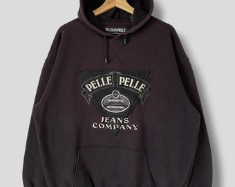 Puede incluir: Una sudadera con capucha gris oscuro con un gran logotipo blanco y negro en la parte delantera. El logotipo dice "Pelle Pelle Jeans Company" y tiene un diseño circular con las palabras "Guaranteed International" en su interior.