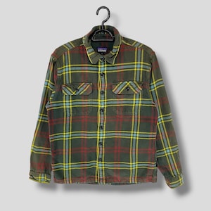 May include: A green, red, yellow and blue plaid flannel shirt with long sleeves and two chest pockets. The shirt has a button-up front and a Patagonia label.