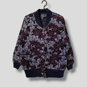 May include: A navy blue bomber jacket with a floral pattern in shades of pink and silver. The jacket has a button closure and two pockets.