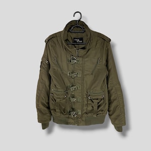 May include: An olive green bomber jacket with multiple pockets and decorative buckles. The jacket has a high collar, shoulder accents, and a ribbed hem and cuffs. The brand name "CECIL" is visible on the label.
