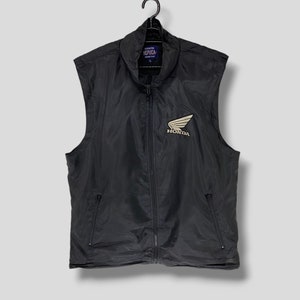 May include: Black sleeveless vest with a zipper closure and two pockets. The vest has a white Honda logo with a red wing on the front.