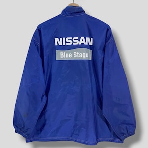 May include: A blue nylon jacket with the word "NISSAN" in white block letters above "Blue Stage" in a white rectangle. The jacket has a stand-up collar and elastic cuffs.