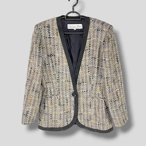 Può includere: Un blazer in tweed grigio e nero con bordino nero e chiusura con un solo bottone. L'etichetta riporta "Christian Dior".