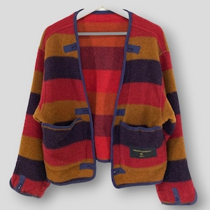 May include: A colorful, open-front jacket with horizontal stripes in red, orange, brown, and purple. The jacket has two front pockets and is trimmed with blue piping. The garment is hanging on a white hanger against a neutral background.