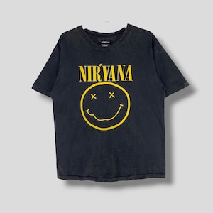 Puede incluir: Camiseta negra con una cara sonriente amarilla y la palabra "NIRVANA" impresa.