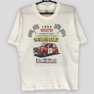 Puede incluir: Camiseta blanca con un gráfico de un Mini Cooper rojo de carreras y el texto "1994 Mini Rallye Team '94 Monte Carlo". La camiseta también incluye el texto "1964-1994 The Mini Is Back".