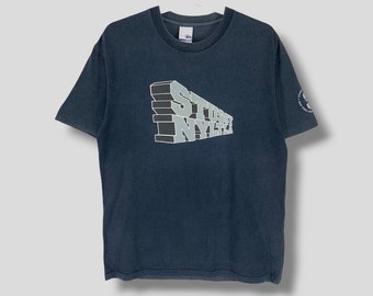 May include: Dark navy blue t-shirt featuring the text "STUSSY NYLH" in a 3D design across the front. The shirt has short sleeves and a crew neck. A small logo is visible on the upper back of the shirt.