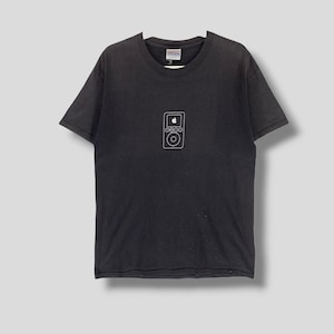 Pode incluir: T-shirt preto com um contorno branco de um iPod e o logotipo da Apple. A camisa tem mangas curtas e gola redonda. O design está centrado no peito.