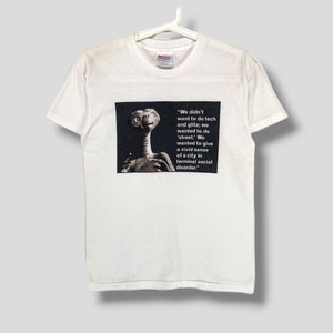 Puede incluir: Camiseta blanca con un gráfico de E.T. el Extraterrestre y texto. El texto dice: "No queríamos hacer tecnología y brillo; queríamos hacer 'calle'. Queríamos dar una vívida sensación de una ciudad en desorden social terminal."