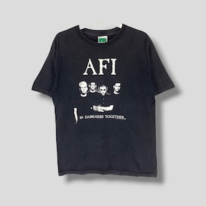 May include: Black t-shirt featuring the band AFI with a graphic of the band members and the text "AFI" above the image and "IN DARKNESS TOGETHER..." below. The shirt is hanging on a white hanger.