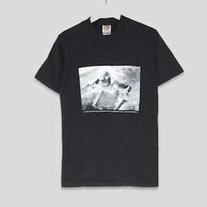 Op de afbeelding: Zwart T-shirt met een grafische print van een vrouw in een zwart-witfoto. De tekst "MUSIC. THE BEAT. THE LIFE OF SOUND. THE ECHOES WE HEAR. THE FEELING WE SHARE. THE POWER OF MUSIC." staat onder de afbeelding.