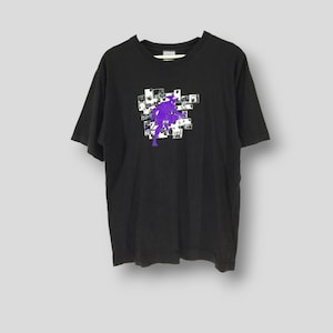 May include: Black t-shirt with a graphic design featuring a purple figure in a dynamic pose, surrounded by a collage of small, white and black images. The shirt is hanging on a white hanger.