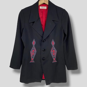 May include: Black blazer with red lining and decorative red and gray embroidered designs on the front. The blazer has a classic collar, three buttons, and long sleeves. The label inside the blazer reads "Kanba Or".