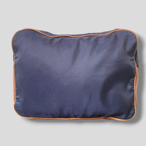 May include: A rectangular navy blue travel bag with a textured surface. The bag is outlined with a thin, light brown trim. The bag is designed for travel and storage.