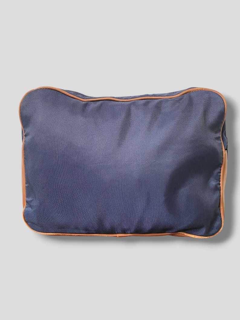May include: A rectangular navy blue travel bag with a textured surface. The bag is outlined with a thin, light brown trim. The bag is designed for travel and storage.