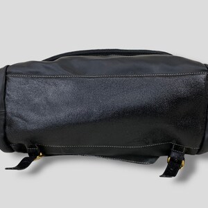 May include: Black leather backpack with a textured finish. The bag features a top zipper, white stitching, and adjustable straps with gold-colored buckles. The bottom of the bag is visible in the image.