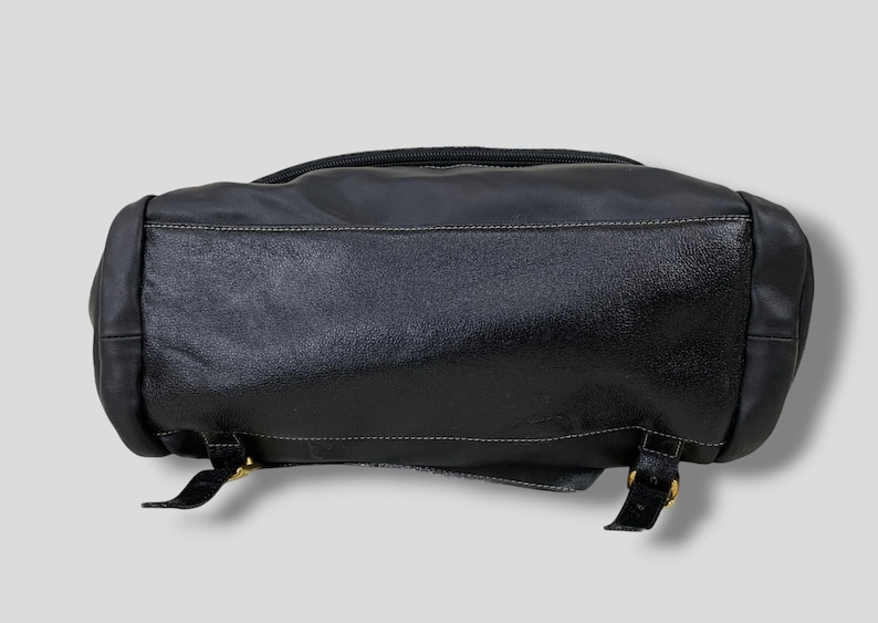 May include: Black leather backpack with a textured finish. The bag features a top zipper, white stitching, and adjustable straps with gold-colored buckles. The bottom of the bag is visible in the image.