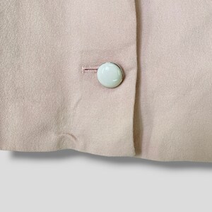 May include: A close-up of a light pink fabric with two white buttons. The buttons are sewn onto the fabric and have a silver rim.