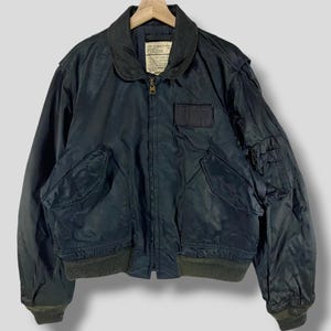 May include: A dark blue bomber jacket with a zipper closure, two front pockets, and a ribbed knit collar, cuffs, and waistband. The jacket has a patch on the left chest with the text "U.S. AIR FORCE".