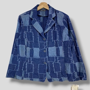 May include: A blue denim blazer with a patchwork design. The jacket features a collared neckline, long sleeves, and three buttons down the front. The patchwork design is made up of various shades of blue denim.