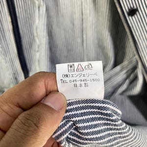 May include: A white tag with black text that reads "(株) エンシェールズ TEL 045-945-1500 日本製". The tag is attached to a blue and white striped fabric.