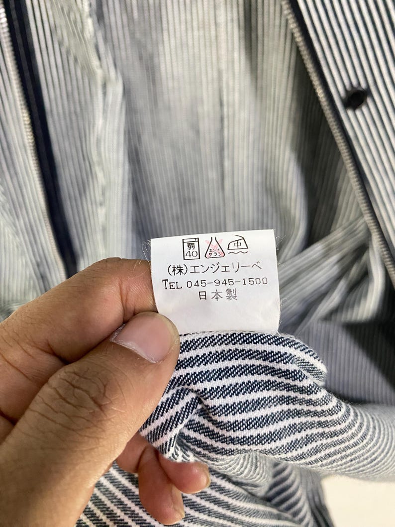 May include: A white tag with black text that reads "(株) エンシェールズ TEL 045-945-1500 日本製". The tag is attached to a blue and white striped fabric.