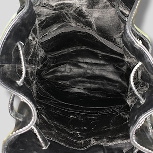 May include: Open view of a black leather backpack interior. The bag has a zippered pocket and multiple compartments. White stitching accents the edges. The leather appears worn, with visible creases and textures.