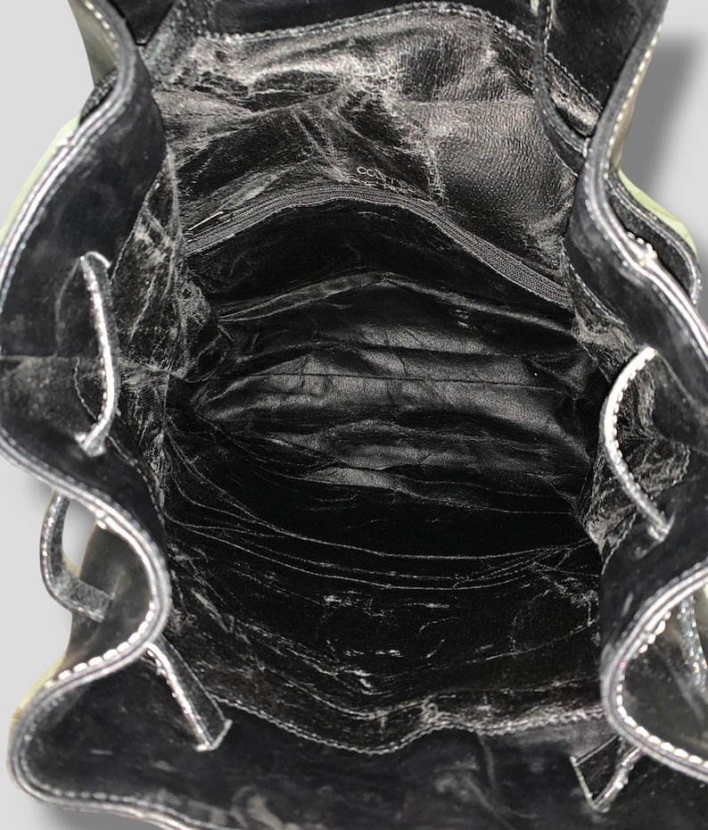 May include: Open view of a black leather backpack interior. The bag has a zippered pocket and multiple compartments. White stitching accents the edges. The leather appears worn, with visible creases and textures.