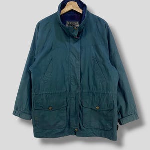 Può includere: Una giacca verde scuro con chiusura a zip e due grandi tasche sul davanti. La giacca ha un'etichetta con la scritta "Pacific Trail" sul lato sinistro del petto.