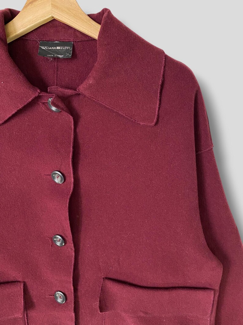 Puede incluir: Una chaqueta de lana color burdeos con cuello, cierre de botones y dos bolsillos de parche. La etiqueta dice "Luciana Zuffi" y "Made in Italy".