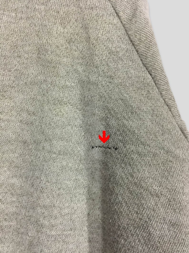 K&ouml;nnte beinhalten: Nahaufnahme eines hellgrauen Stoffes mit einem kleinen Riss. Der Stoff hat ein strukturiertes Aussehen und eine sichtbare Naht. Der Riss ist eine horizontale Linie aus gebrochenen F&auml;den.