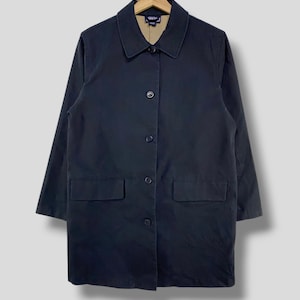 May include: A navy blue coat with a collared neckline, three buttons, and two front pockets. The coat is hanging on a wooden hanger. The interior lining of the collar is tan.