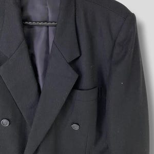 May include: A black double-breasted blazer with a notch lapel and four buttons. The blazer has a pocket on the left side.