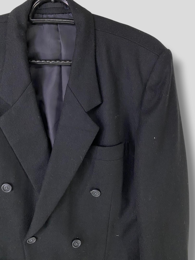 May include: A black double-breasted blazer with a notch lapel and four buttons. The blazer has a pocket on the left side.