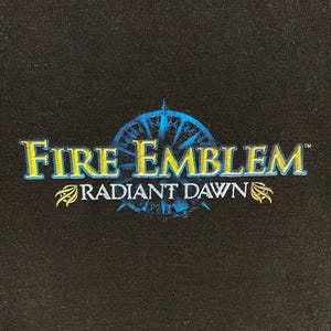 May include: Black fabric featuring the text "Fire Emblem Radiant Dawn" in gold and blue. The design includes a compass rose and decorative elements, suggesting a video game or fantasy theme. The text is stylized.