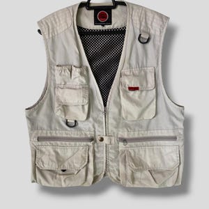 Puede incluir: Un chaleco utilitario beige con múltiples bolsillos y cierre de cremallera. El chaleco tiene un panel de malla en la espalda y un logotipo rojo en la parte delantera.
