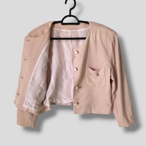 May include: A pale pink blazer with long sleeves and a button closure. The blazer has a single pocket on the right side and a white lining.