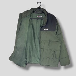 May include: Olive green puffer jacket with a black panel on the upper chest and collar. The jacket features the "FILA" logo in white on the chest. The jacket is hanging on a black hanger.