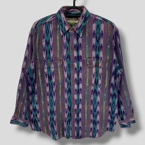May include: A long-sleeved button-down shirt with a colorful, vertical patterned design in shades of purple, teal, and yellow. The shirt has two chest pockets and is hanging on a black hanger. The fabric appears to be a woven material.