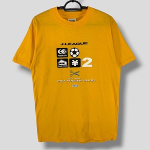 May include: Mustard yellow t-shirt with a black graphic design featuring the text "J.LEAGUE", a football, and the number "2". The shirt also includes the text "LET'S MAKE PRO SOCCER CLUB!" and the SEGA logo.