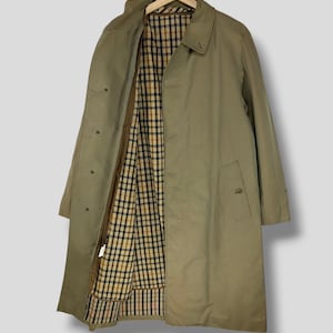 May include: A beige trench coat with a plaid lining. The coat has a button closure and a single pocket on the left side.