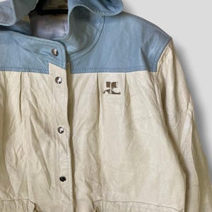 Puede incluir: Una chaqueta de cuero blanca y azul claro con capucha. La chaqueta tiene cierre de botones y cintur&oacute;n. La chaqueta tiene un logotipo en la parte delantera que dice "JC".