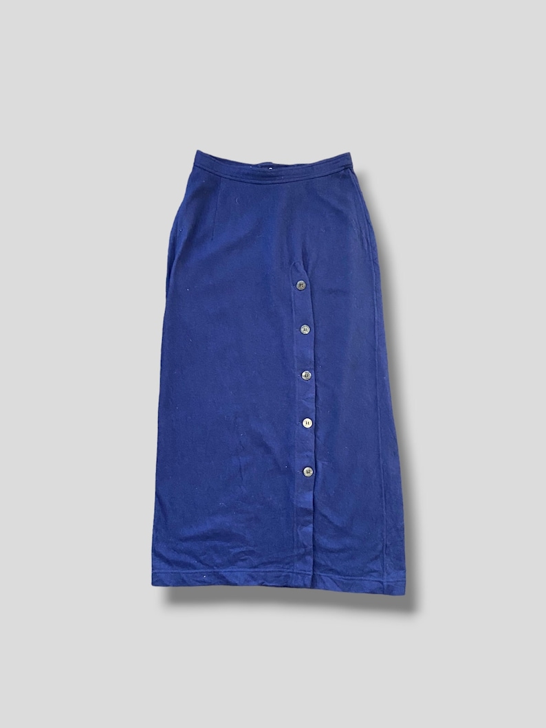 Puede incluir: Falda larga azul marino con cierre de botones en el lado izquierdo. La falda tiene un dise&ntilde;o simple y cl&aacute;sico, adecuado para diversas ocasiones. Los botones son de color claro, proporcionando contraste con la tela azul oscura.