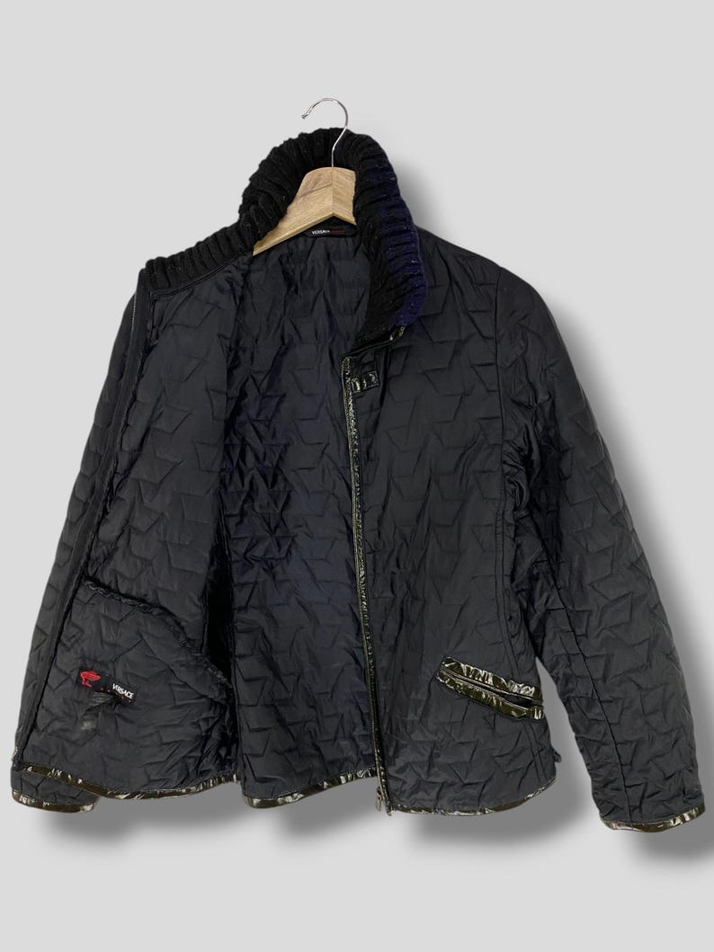 May include: A black quilted jacket with a zipper closure and a black knit collar. The jacket has a star-shaped pattern and a small red label with the word "VERSACE" on the left side.