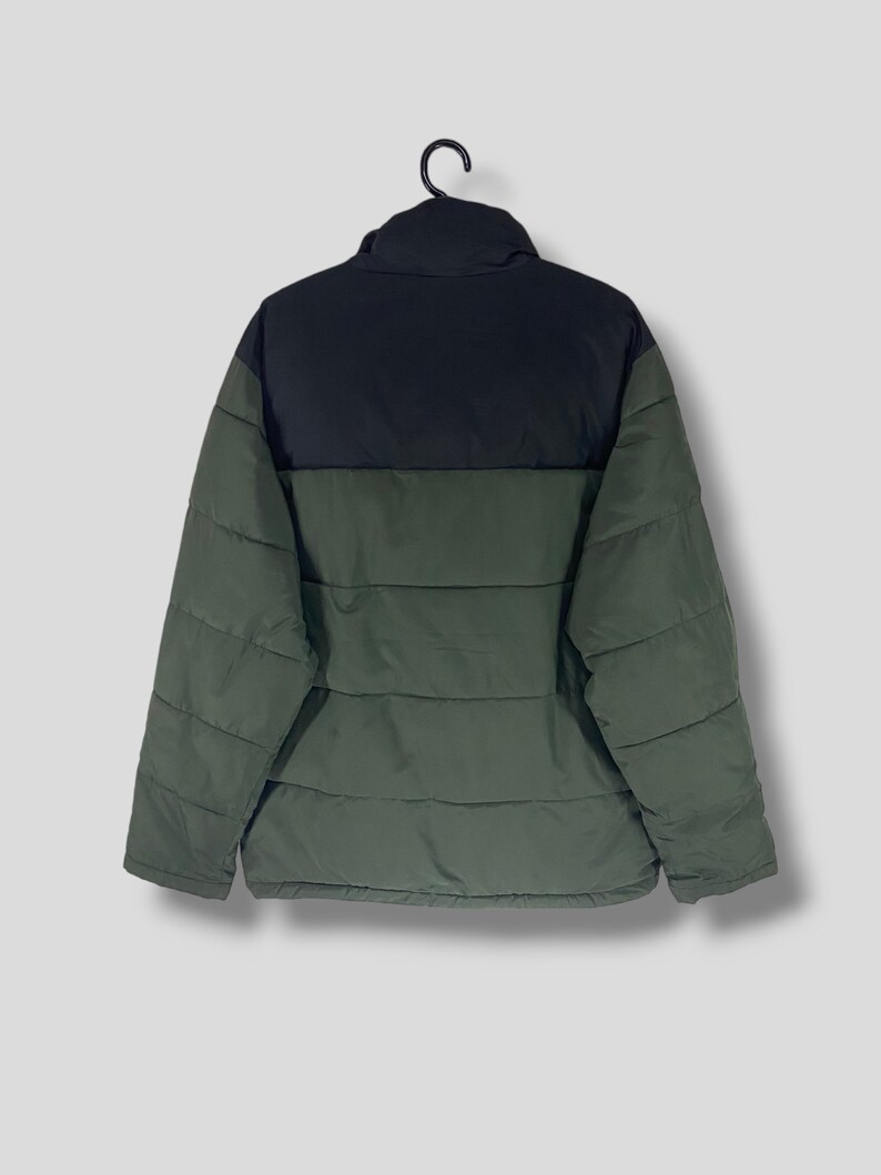 May include: A two-tone puffer jacket in black and olive green, hanging on a black hanger. The jacket has a high collar and horizontal quilted stitching. The back view shows the jacket's design and construction.