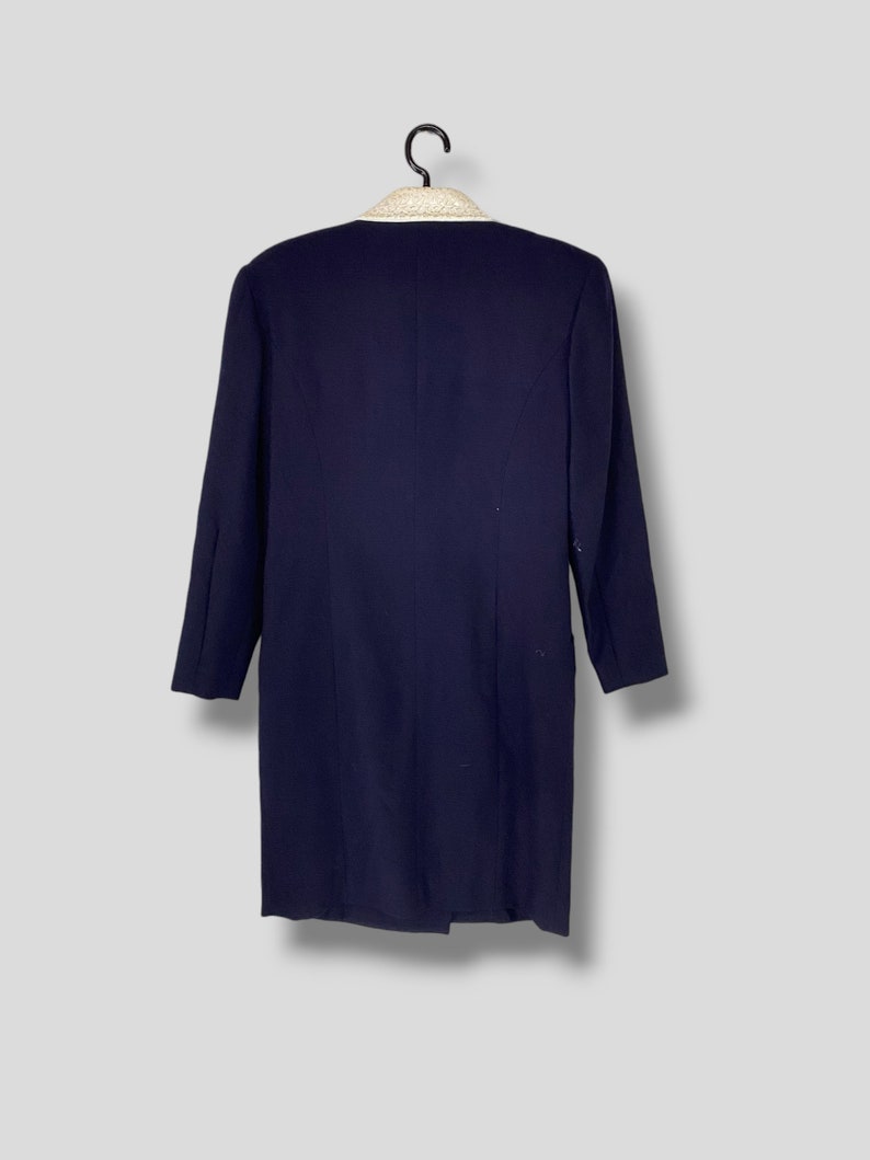 Puede incluir: Una chaqueta azul marino con cuello blanco y ribete de cuentas. La chaqueta tiene mangas largas y un cierre de bot&oacute;n &uacute;nico.