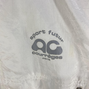 K&ouml;nnte beinhalten: Wei&szlig;e Nylonjacke mit dem Text "sport futur" und "courr&egrave;ges paris" in Grau. Die Jacke hat ein Logo mit den Buchstaben "ac" in einer stilisierten Schriftart. Sie hat einen Knopfverschluss.