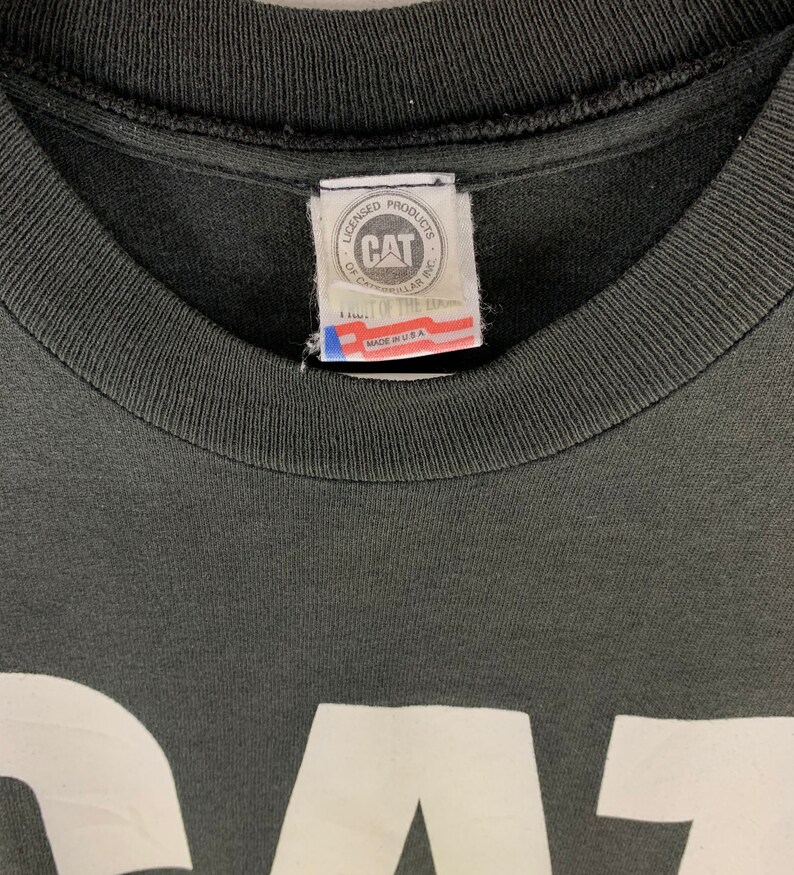 May include: Close-up of a black t-shirt with a white graphic. The shirt's collar and tag are visible. The tag reads "CAT" and "Made in USA". The shirt is made of a soft, comfortable material.